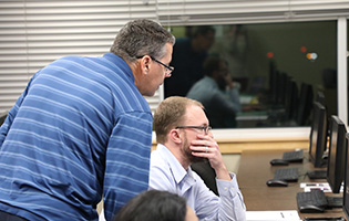 Man Standing Over Another Man Looking at Computer