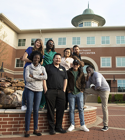 Group of eight students smiling and posing by the fountain in front of the student center
