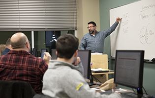 Teacher Pointing to Board In Front of a Class