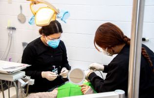 Two Female Students Bent Over a Patient