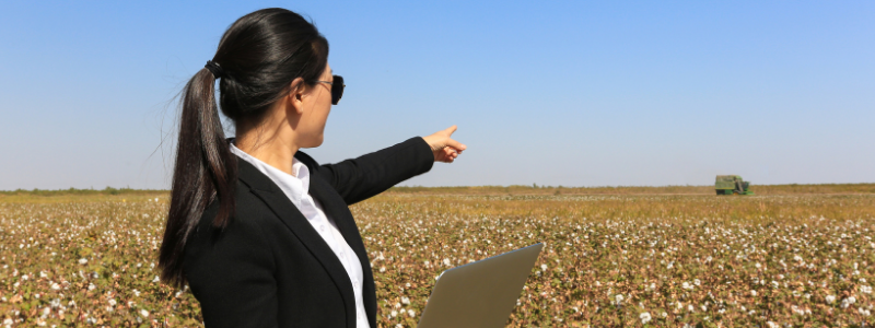 Woman Holding Laptop and Pointing to a Field of Crops