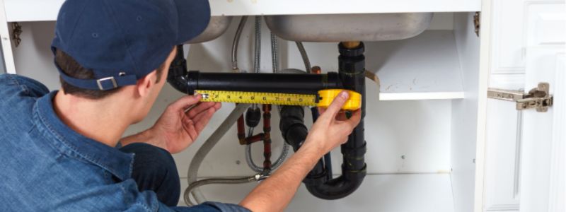 Plumber Measuring a Pipe Under a Sink