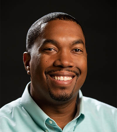 smiling black man wearing a sea green polo against a black background