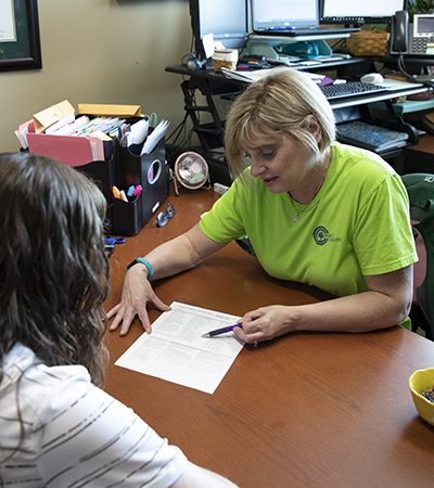 Female advisor with blonde hair pointing at a piece of paper while talking to a female student with brown hair