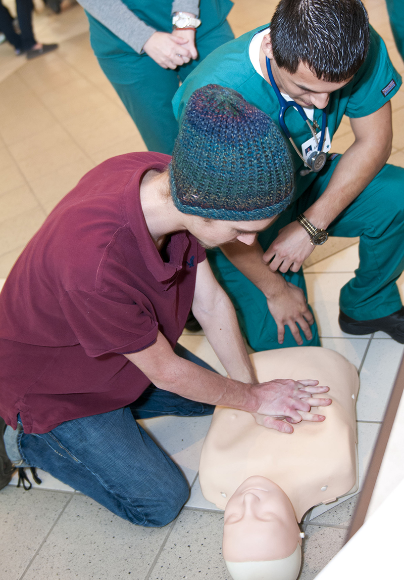Two male respiratory therapy students practice chest compressions on a dummy
