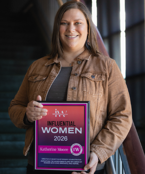 Woman in front of staircase holding a plaque that reads 2026 Influential Woman