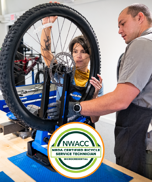 Man and woman working on a bicycle on a work bench in a classroom.