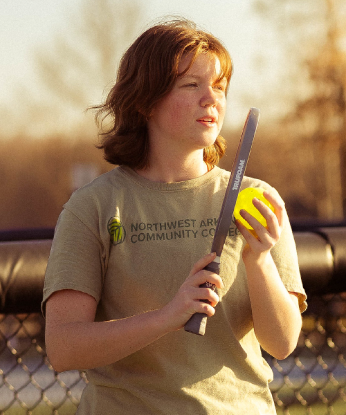 Woman in NWACC shirt holding pickleball and paddle